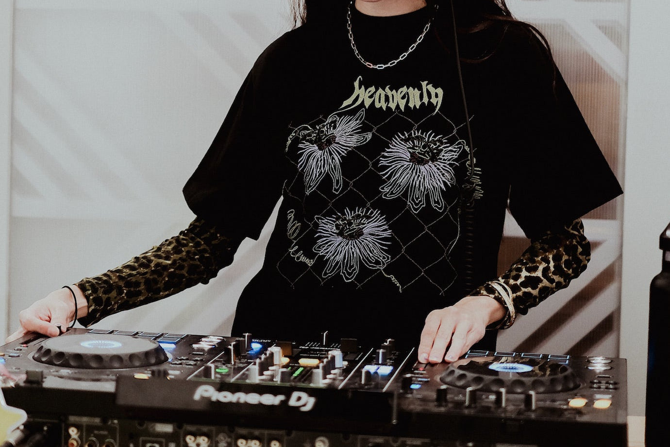 Person DJing with headphones on, surrounded by music equipment and drinks.