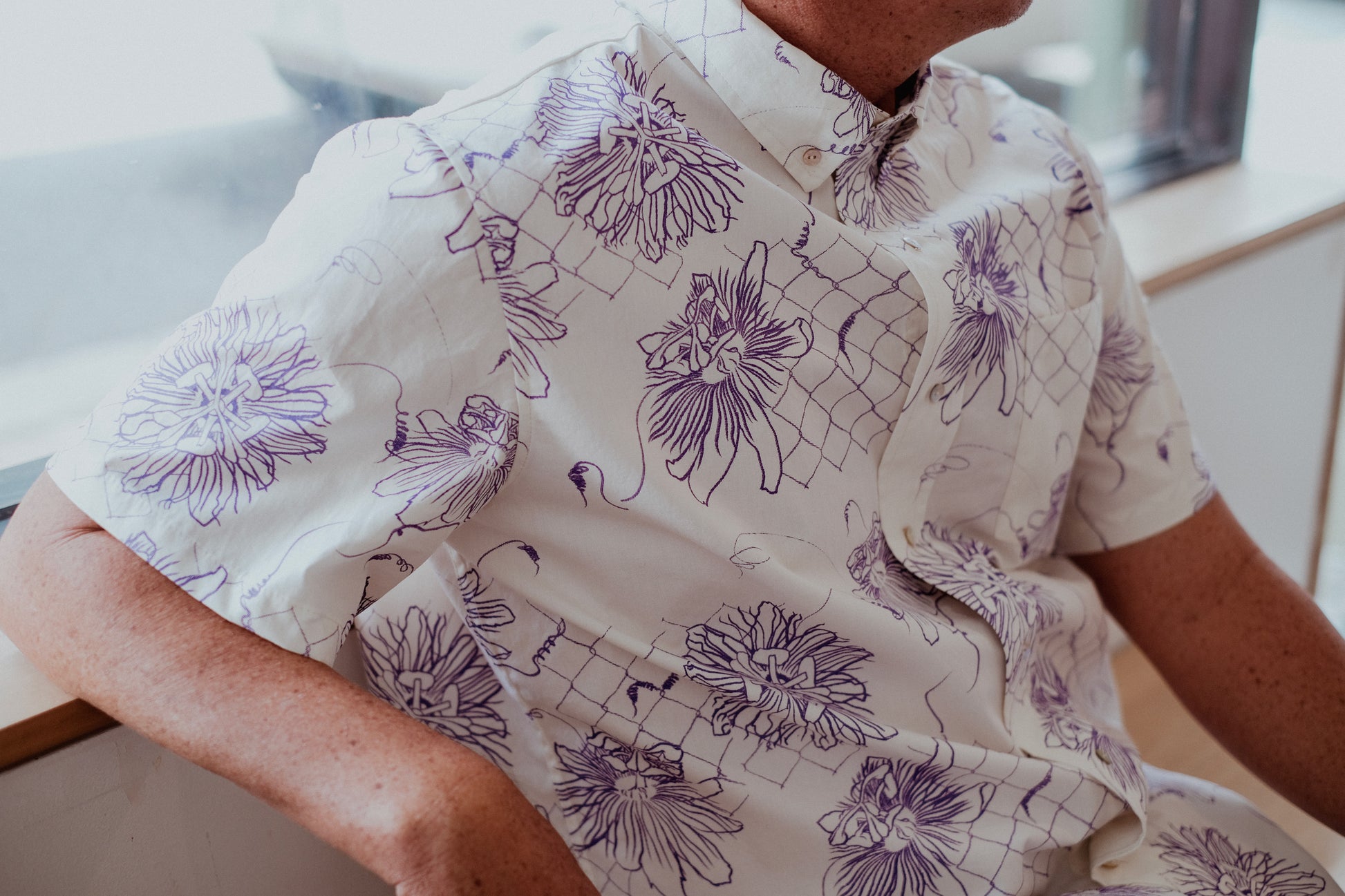 Person wearing a white shirt with purple floral patterns sitting.