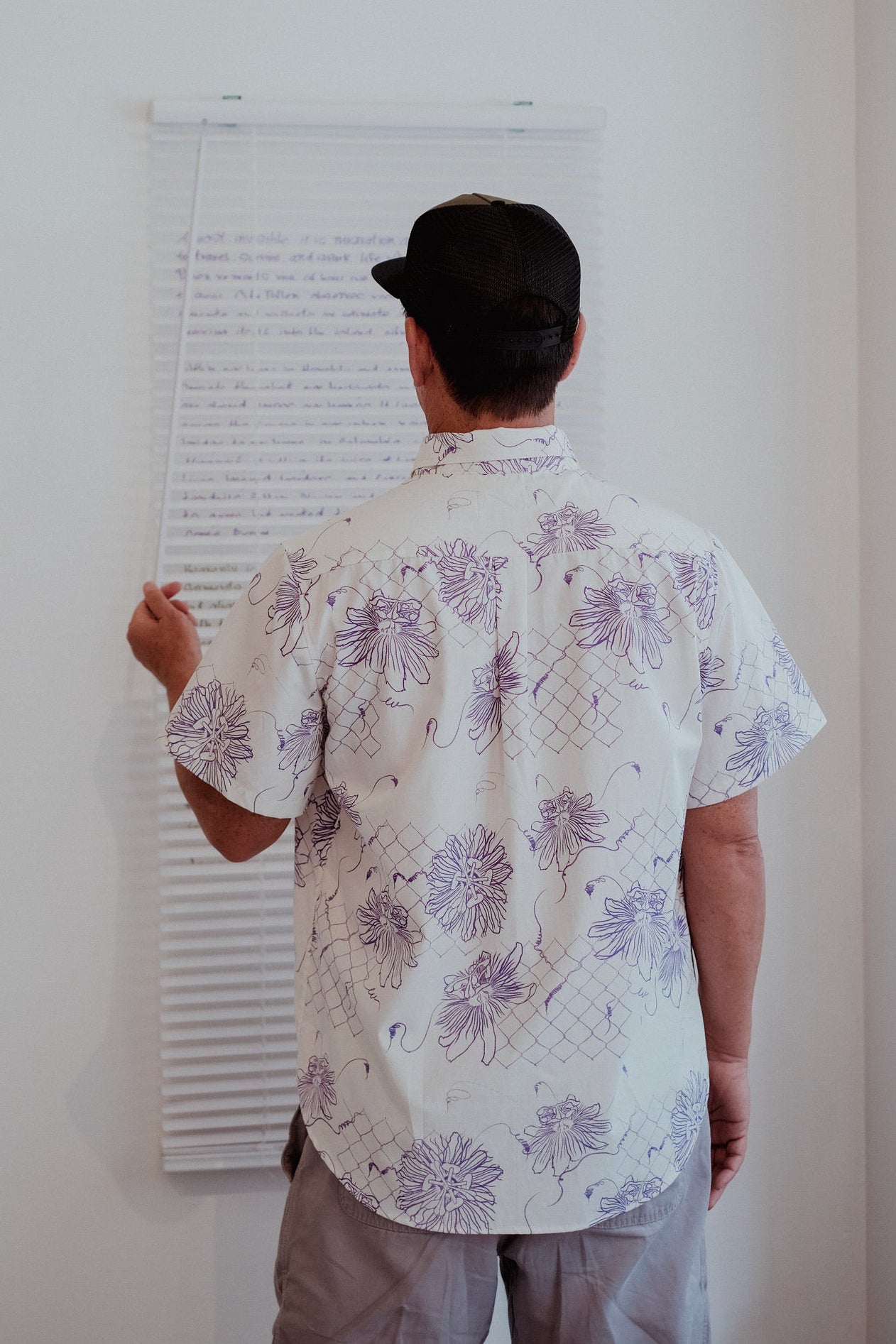 Person wearing a floral shirt and cap, standing in front of a whiteboard with text on it.