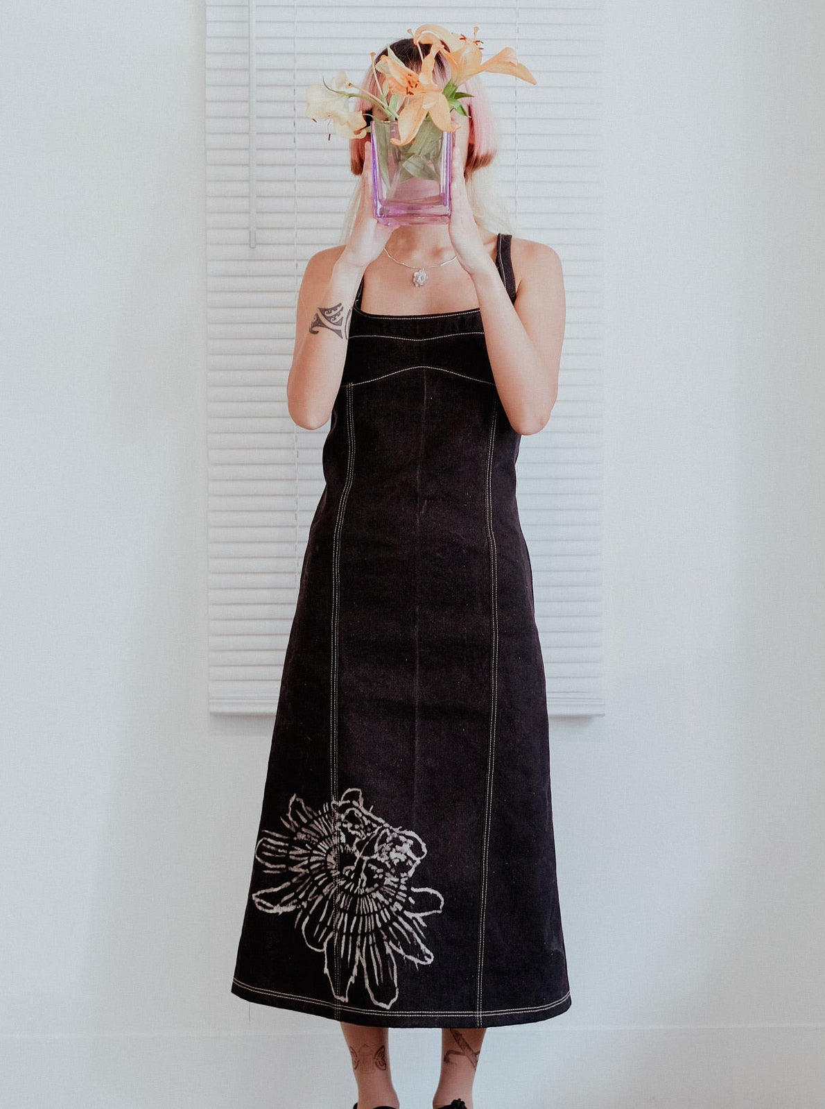 Person wearing a black dress with floral embroidery in front of a white wall.